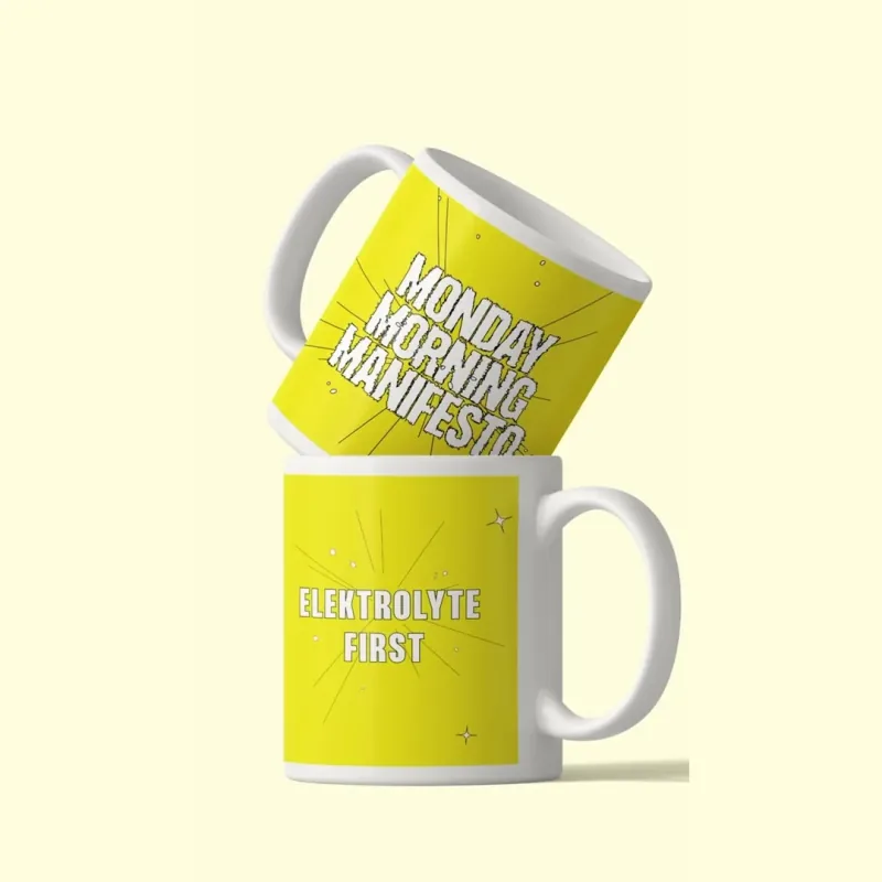 Zwei gelbe Keramiktassen mit den Sprüchen Monday Morning Manifesto und Elektrolyte First
