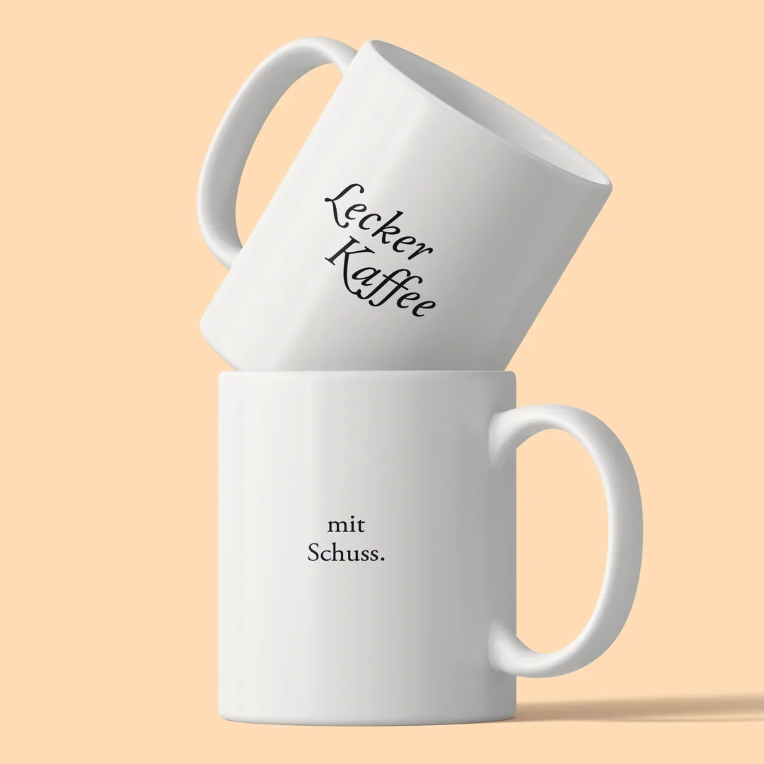 Zwei gestapelte Lecker Kaffee Tassen vor pfirsichfarbenem Hintergrund, oben Lecker Kaffee, unten mit Schuss.