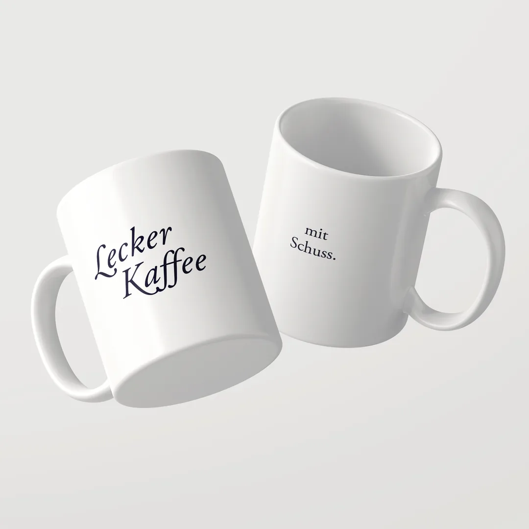 Zwei weiße Lecker Kaffee Tassen von Studio SaySay, eine zeigt Lecker Kaffee, die andere mit Schuss.