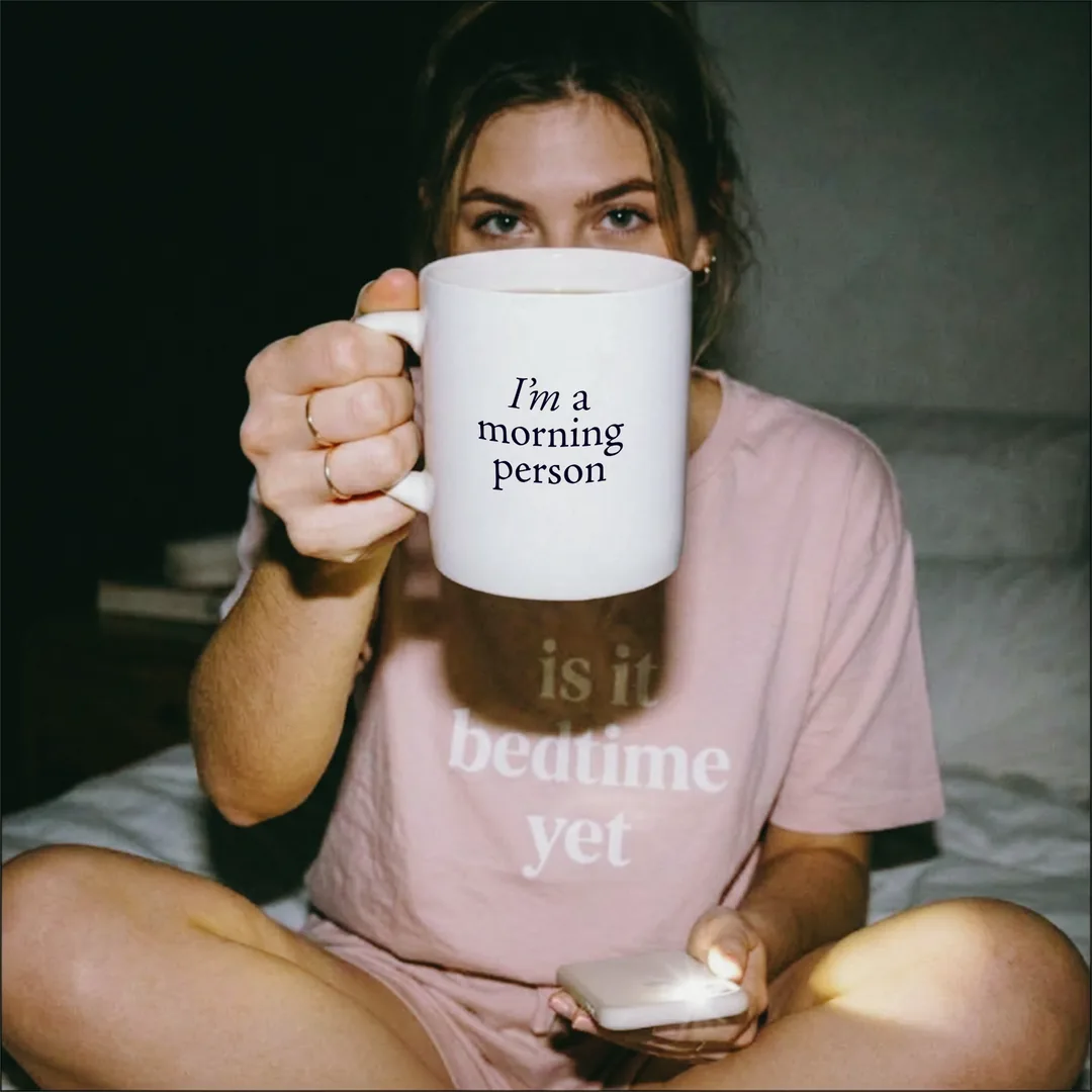 Abends im Bett: Eine Person hält die I’m a Morning Person Tasse vors Gesicht